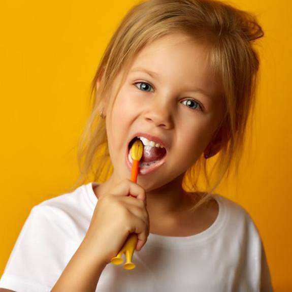 young girl brushing her teeth against a yellow-orange background 