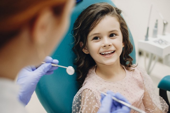 A young girl smiling while seated and waiting for a children’s dentist in Grand Prairie to perform a regular checkup