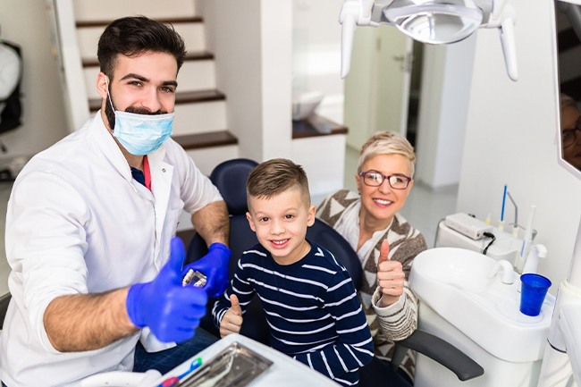 A dentist, mother, and son all give thumbs up after a successful checkup in Grand Prairie