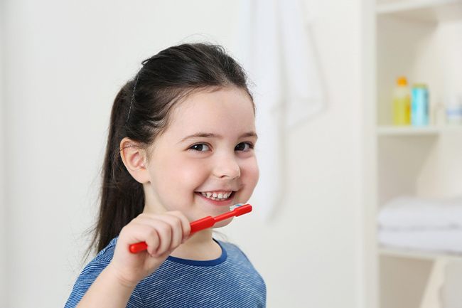 A young girl with dark hair uses a manual toothbrush to clean her teeth at home