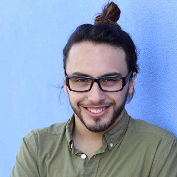 young man in green shirt smiling against blue wall