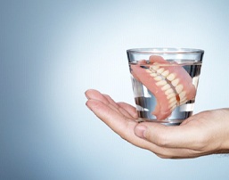 hand holding a glass of water with full dentures soaking in it