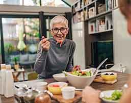 Woman smiling while eating lunch with friend in kitchen