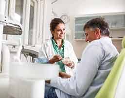 Smiling dentist showing patient model of teeth