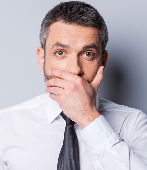 Man in need of tooth replacement covering his mouth