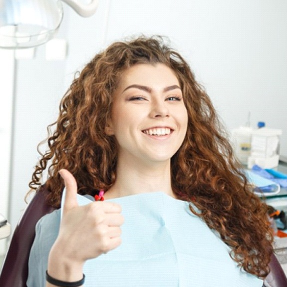 smiling young woman giving thumbs up in dental chair
